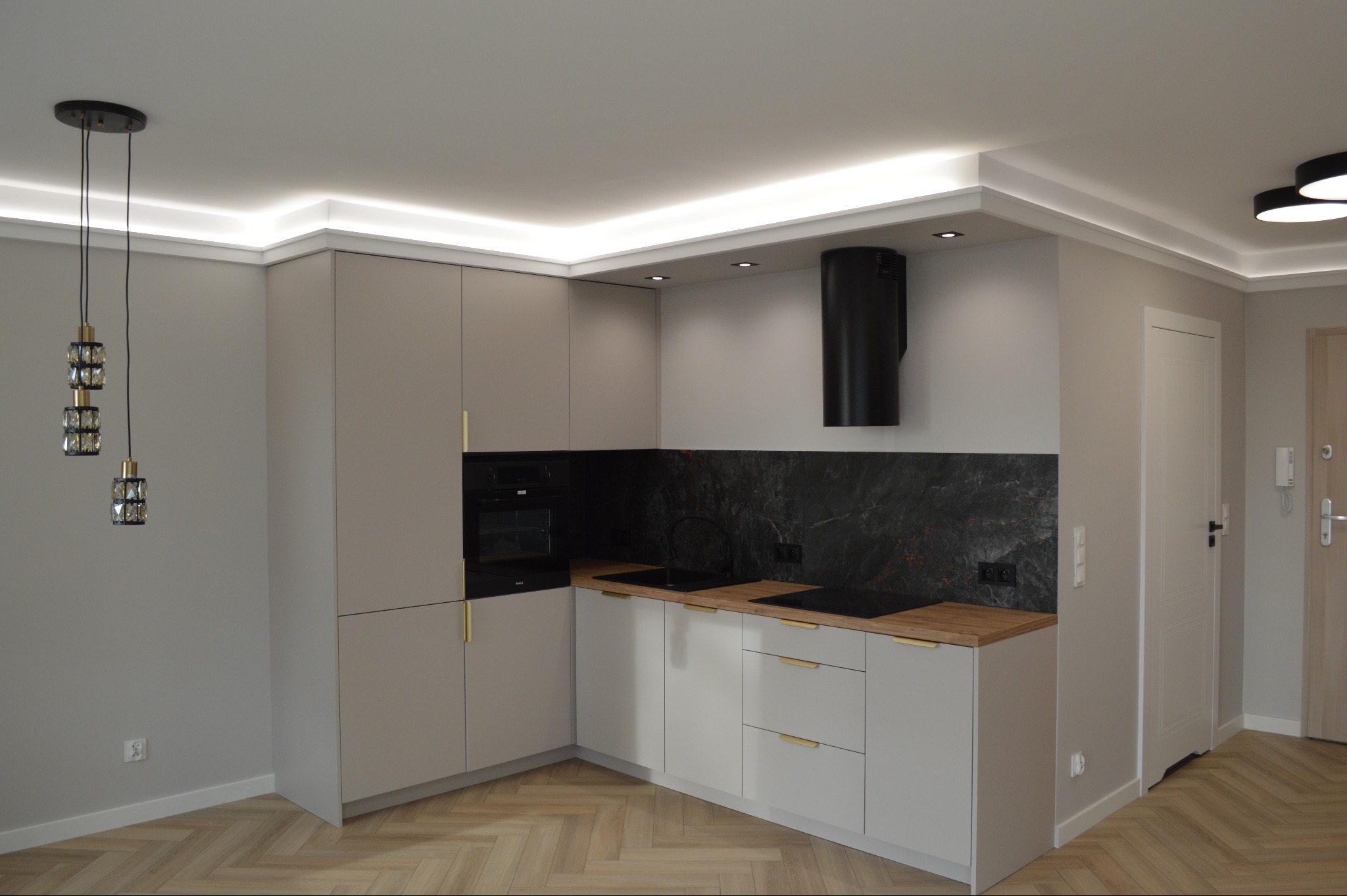 Nowoczesna kuchnia w odcieniach szarości z drewnianym blatem, czarnym okapem i designerskimi lampami wiszącymi. Uwagę zwraca oświetlenie LED podszafkowe i na suficie.