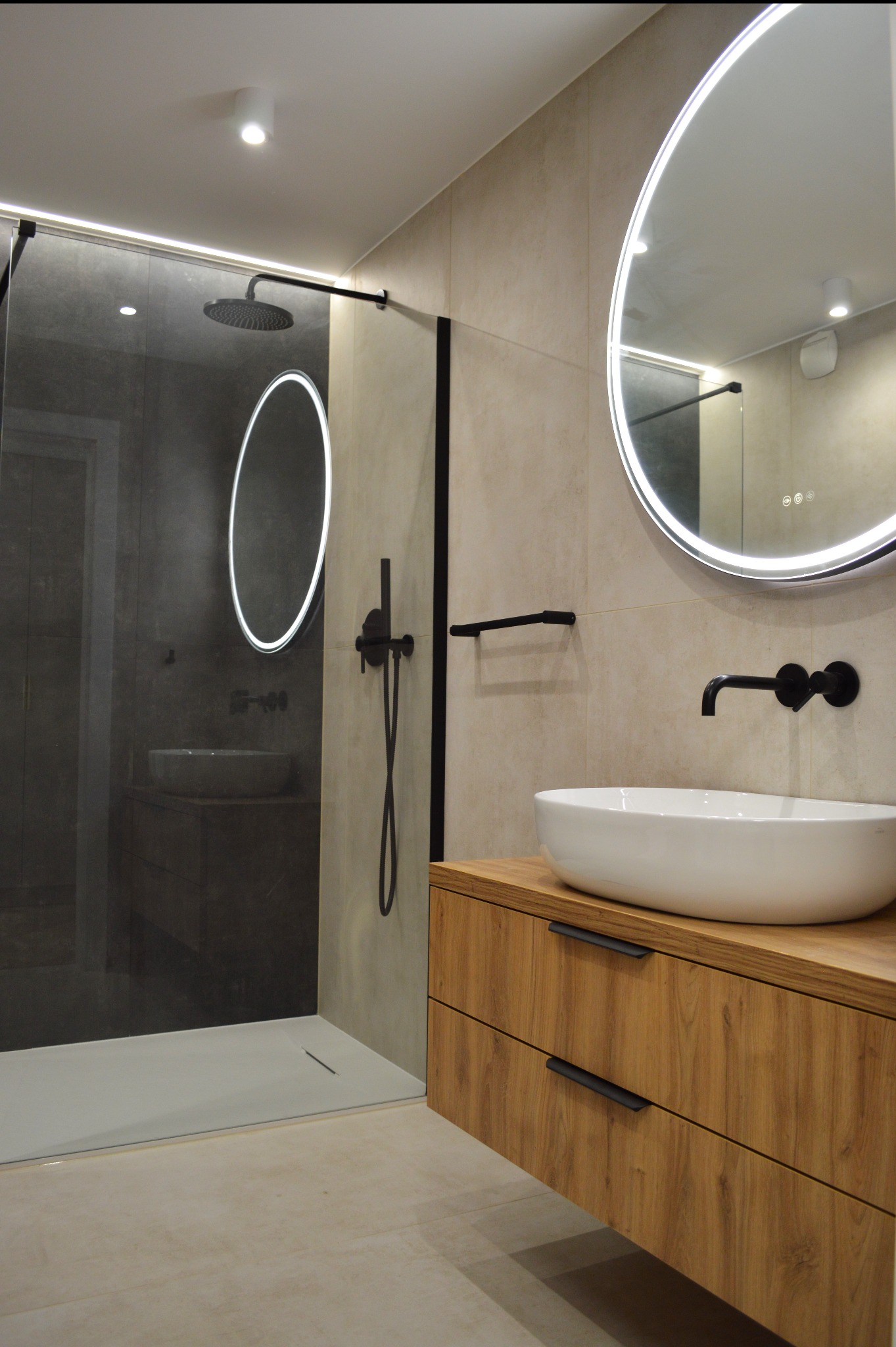 Nowoczesna łazienka z kabiną typu walk-in, umywalką nablatową na drewnianej szafce i okrągłym lustrem z podświetleniem LED. Armatura w kolorze czarnym.