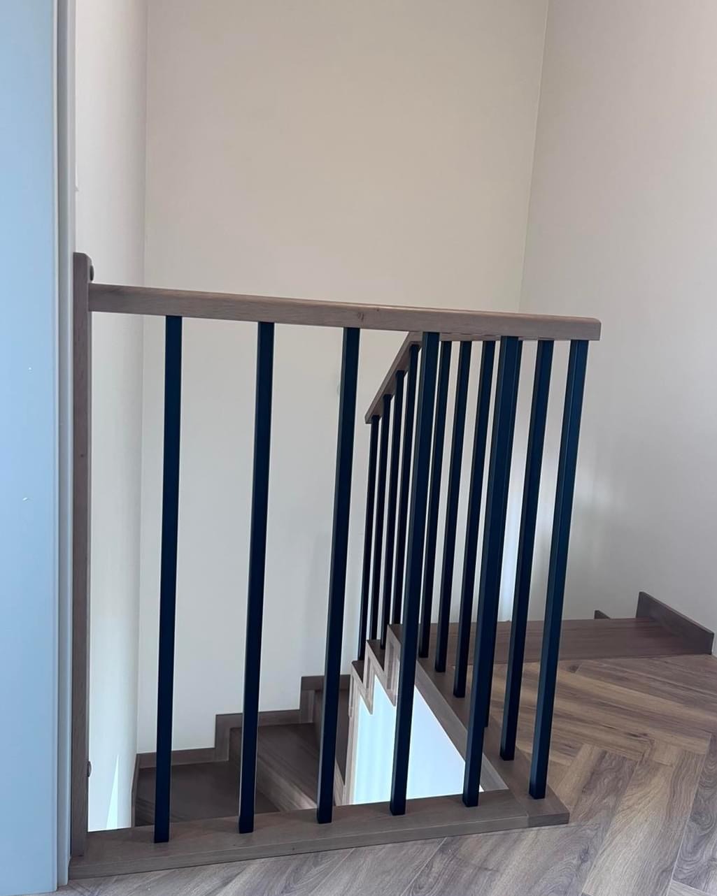 Nowoczesne schody z drewnianymi stopniami i czarną, metalową balustradą z drewnianym poręczą, widok z góry, parkiet ułożony w jodełkę.