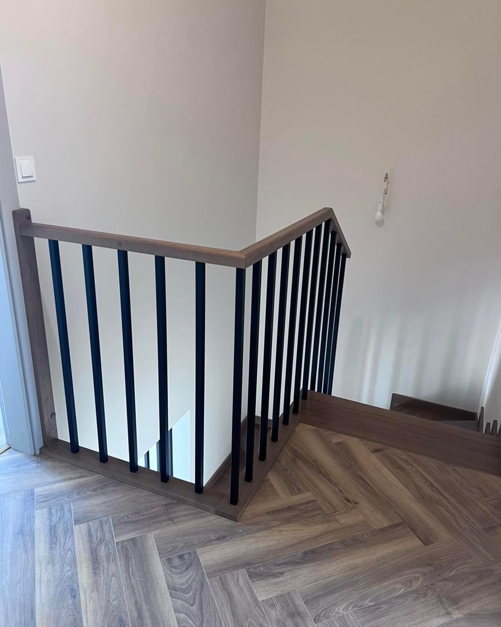 Nowoczesne schody z drewnianymi stopniami i czarną, metalową balustradą. Parkiet ułożony w jodełkę. Minimalistyczny design.