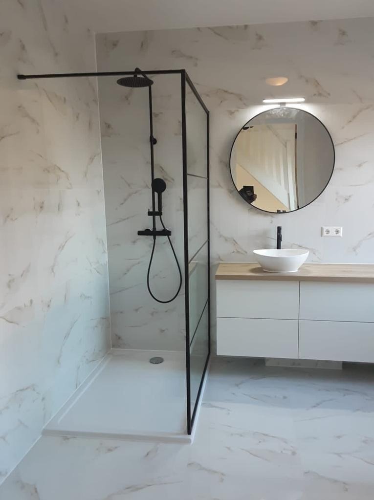 Nowoczesna łazienka z kabiną typu walk-in, czarną armaturą i okrągłym lustrem. Marmurowe płytki na ścianach i podłodze, biała szafka pod umywalką z drewnianym blatem.