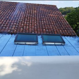 USŁUGI BUDOWLANE WOJCIECH WALA - Dach z dwoma oknami połaciowymi po obróbkach blacharskich w Jarocinie, widok z góry. Czerwona dachówka w tle i fragment zieleni.