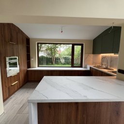 Kreator Twojej Przestrzeni - Nowoczesna kuchnia z wyspą i drewnianymi frontami, marmurowym blatem, oświetleniem LED i widokiem na ogród przez okno.