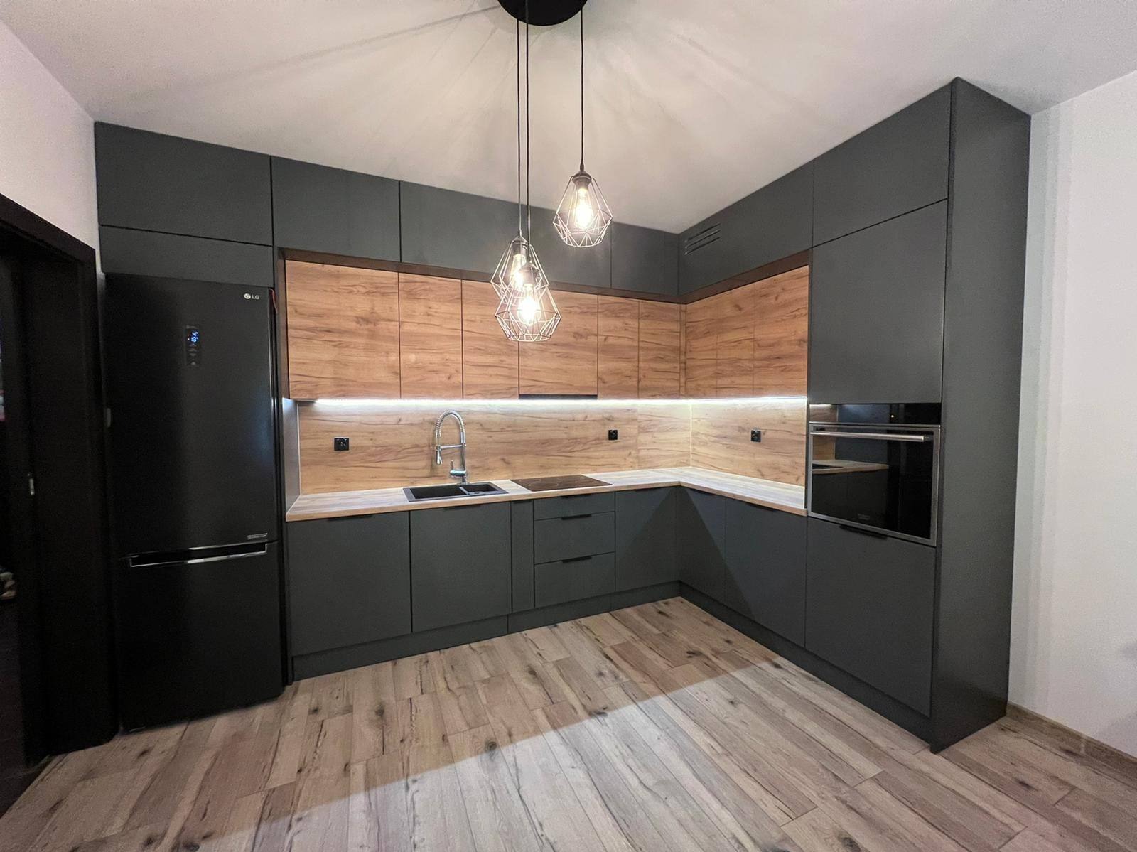 Nowoczesna kuchnia na wymiar: grafitowe szafki dolne i drewnopodobne górne, podświetlenie LED, wiszące lampy druciane i czarna lodówka LG.