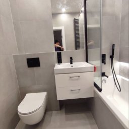 Andrii Derevianko - Nowoczesna łazienka w szarościach: podwieszana toaleta, biała szafka z umywalką, czarna armatura i kabina prysznicowa z lustrem. Minimalistyczny design.