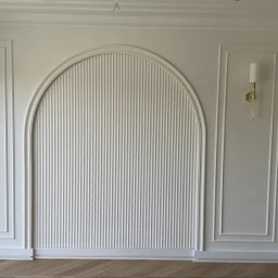 Andrii Derevianko - Biała ściana z dekoracyjnymi listwami, w tym łukowatą, pionowo żłobkowaną wnęką. Dwa kinkiety z abażurami po bokach. Parkiet ułożony w jodełkę.