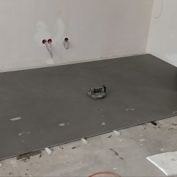 Andrii Derevianko - Wyrównana, szara wylewka samopoziomująca na podłodze w trakcie prac wykończeniowych. Widoczne przewody elektryczne i hydrauliczne w ścianie.