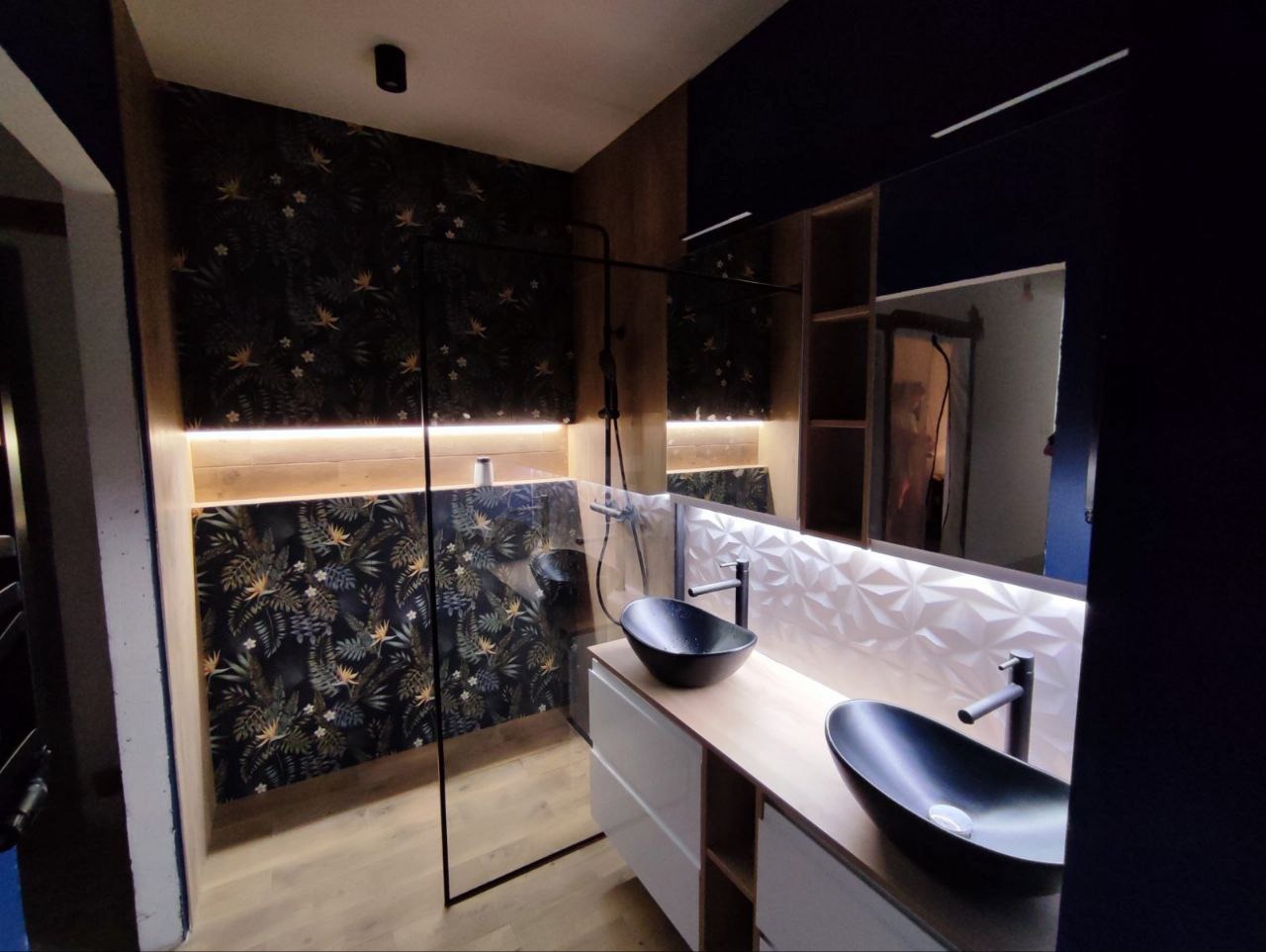 Nowoczesna łazienka z czarnymi umywalkami nablatowymi, wzorzystą tapetą i oświetleniem LED. Kabina prysznicowa typu walk-in z czarnymi profilami.