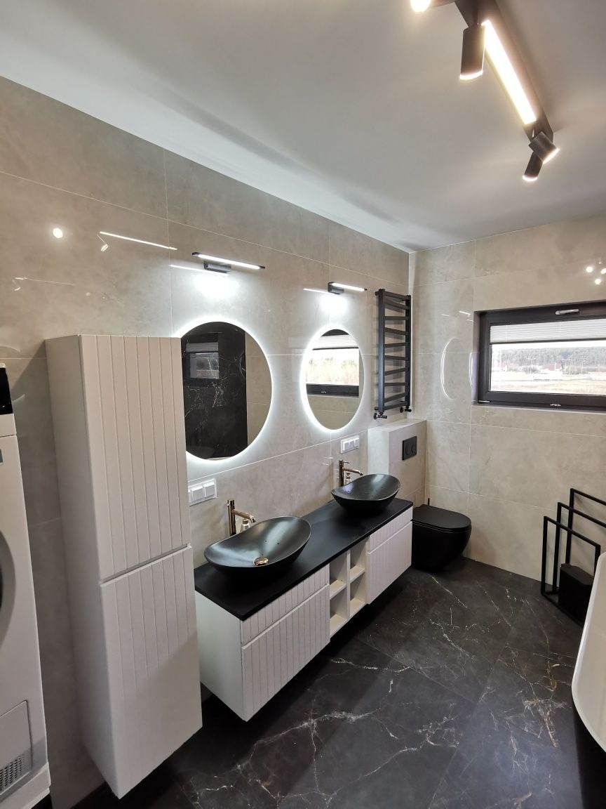 Nowoczesna łazienka w Markach z czarnymi umywalkami i okrągłymi lustrami z podświetleniem LED. Płytki imitujące marmur na podłodze i ścianach.