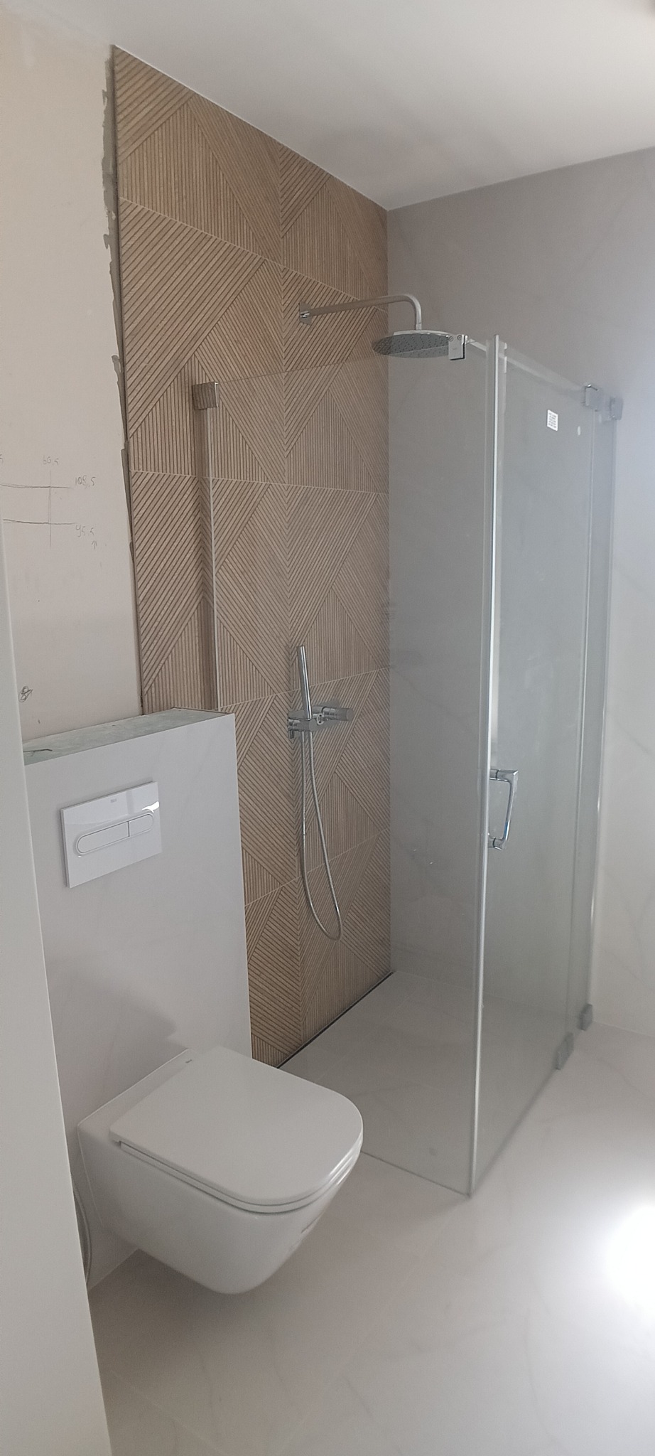 Nowoczesna łazienka z kabiną prysznicową typu walk-in i podwieszaną toaletą. Na ścianie dekoracyjne płytki w geometryczny wzór. Minimalistyczny design.