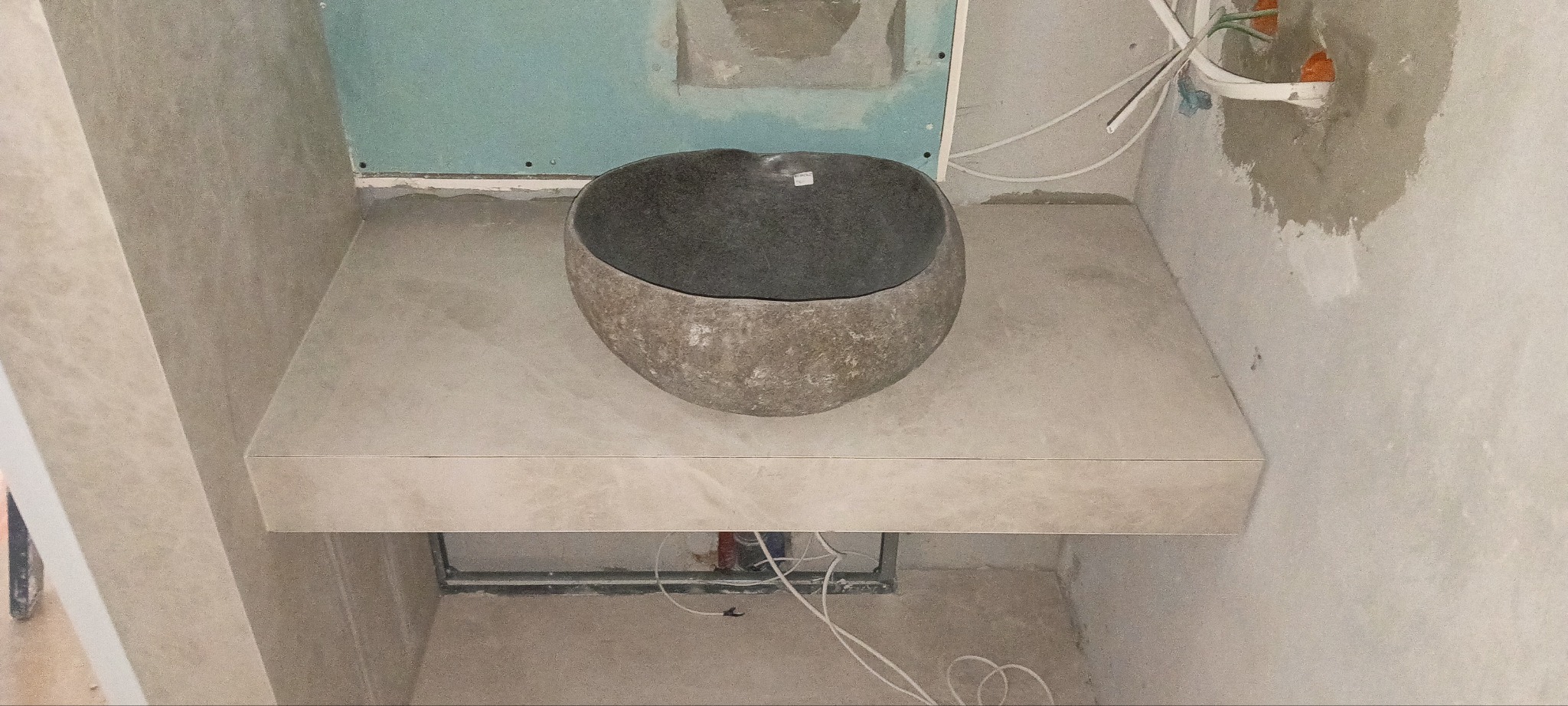 Kamienna umywalka w kształcie misy na blacie z płytek w surowej łazience w trakcie wykończenia. Widoczne instalacje i płyty karton-gips.