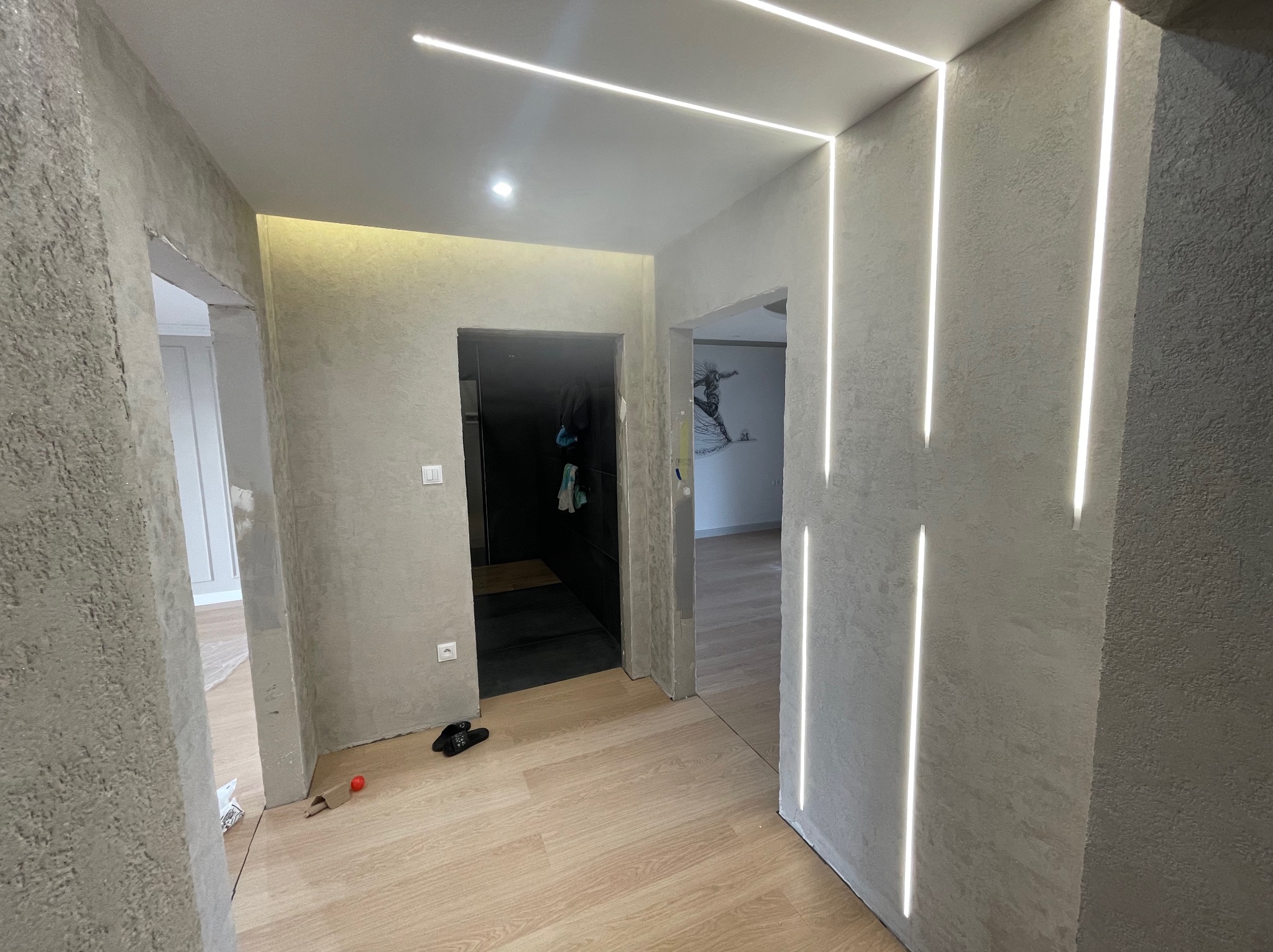 Wnętrze po wykończeniu: ściany z fakturą, podłoga drewniana, oświetlenie LED w pionowych liniach na ścianie. Widoczne drzwi do innych pomieszczeń.