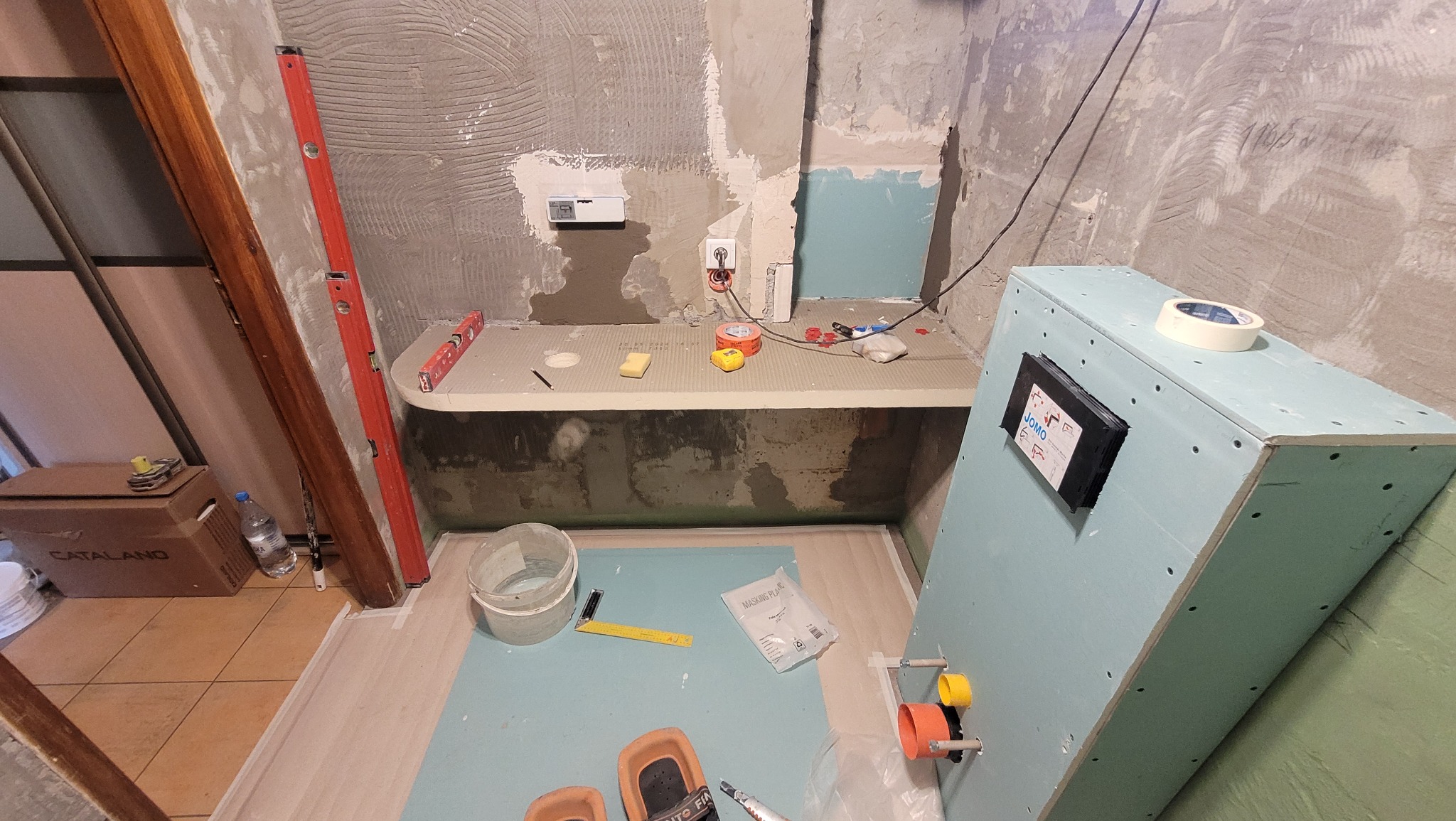 Niedokończona łazienka w trakcie prac remontowych: widoczne surowe ściany, instalacje, płyty gipsowe, poziomica, narzędzia i akcesoria budowlane.