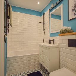 Twój Dom - Wykończona łazienka w bieli i błękicie: białe płytki imitujące cegłę, wzorzysta podłoga, biała szafka z umywalką i czarna armatura. Minimalistyczny styl.