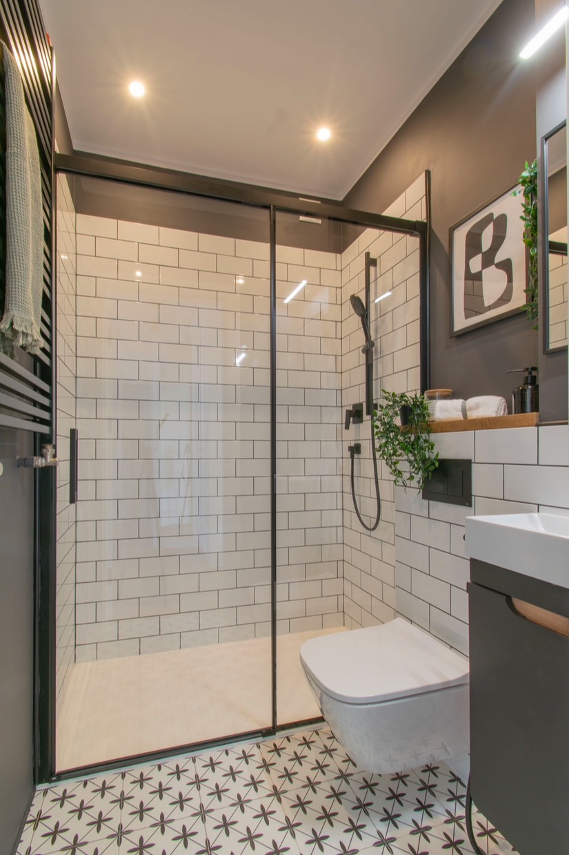 Nowoczesna łazienka z kabiną prysznicową typu walk-in, białe płytki imitujące cegłę, wzorzysta posadzka i czarne akcenty. Minimalistyczny design.