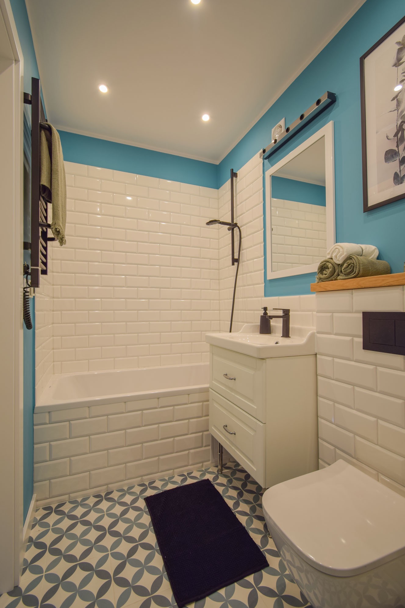 Wykończona łazienka w bieli i błękicie: białe płytki imitujące cegłę, wzorzysta podłoga, biała szafka z umywalką i czarna armatura. Minimalistyczny styl.