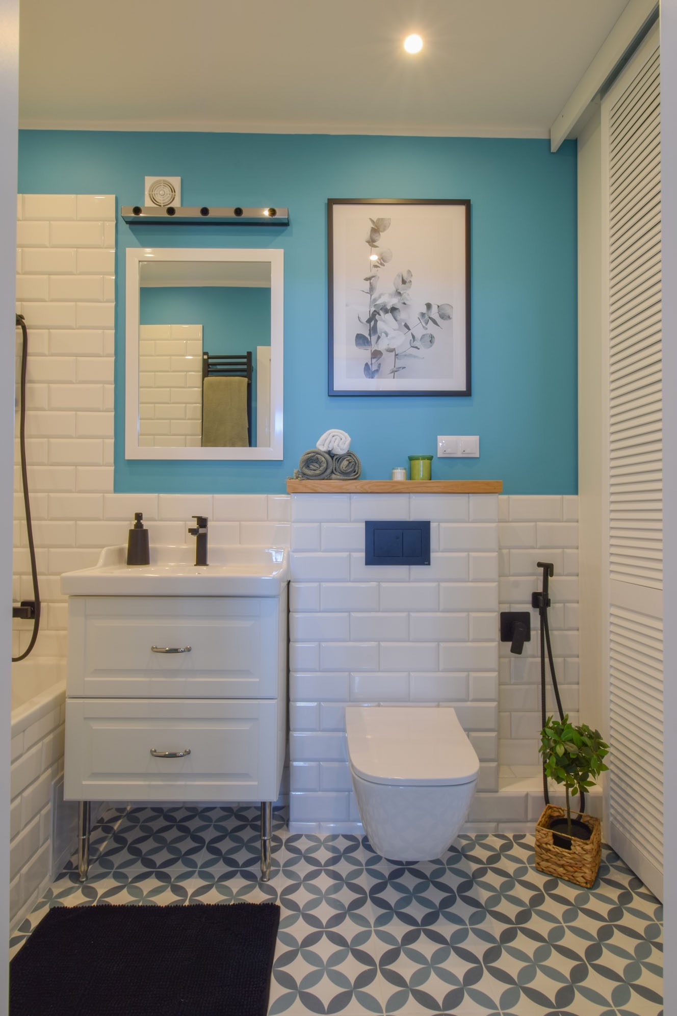 Estetyczna aranżacja łazienki z turkusową ścianą, białymi płytkami imitującymi cegłę i szafką umywalkową na metalowych nóżkach. Uwagę przykuwają wzorzyste płytki podłogowe.