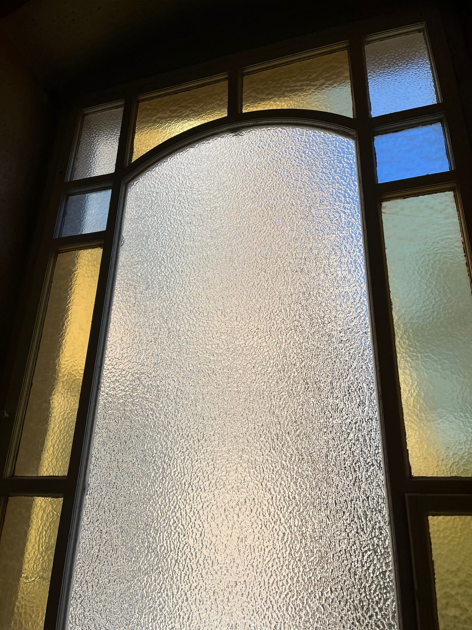 Arched window with textured glass and colored panes in gold and blue, viewed from below, creating a bright, airy feel.