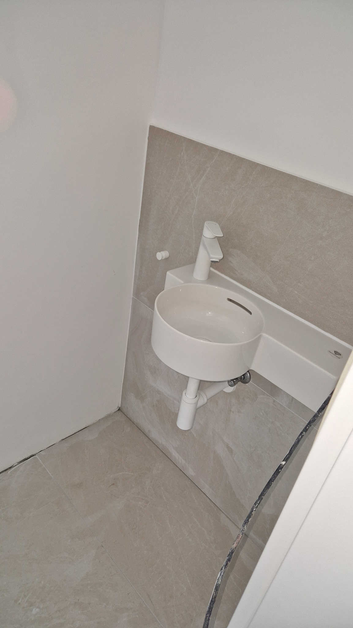 Nowoczesna, okrągła umywalka z białą armaturą, zamontowana na beżowych płytkach w łazience. Minimalistyczny design, świeżo po instalacji.