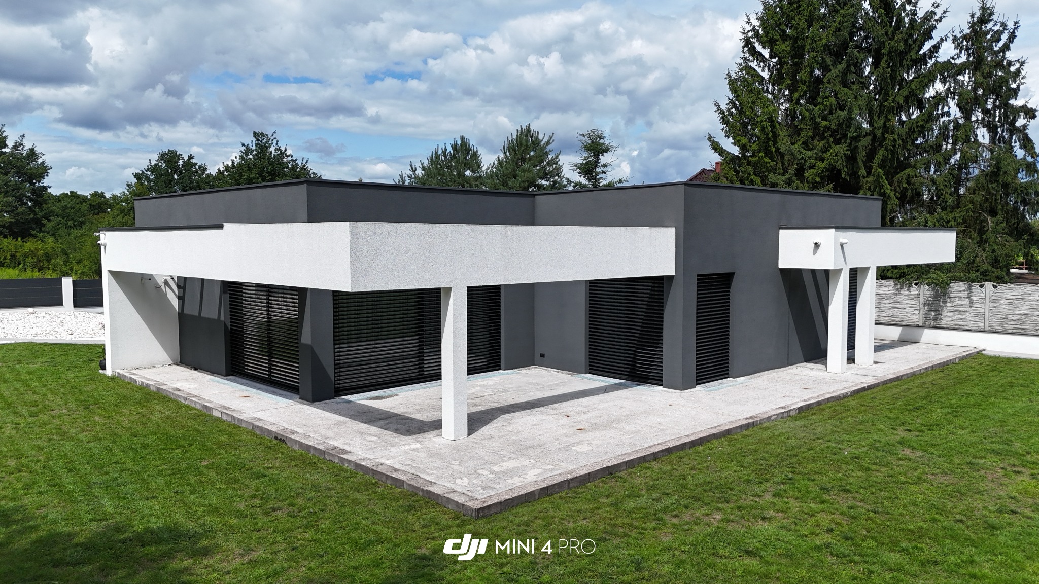 Nowoczesny dom jednorodzinny z płaskim dachem i tarasem w Słupcy, sfotografowany z drona. Minimalistyczna architektura, szara elewacja, białe elementy konstrukcyjne.