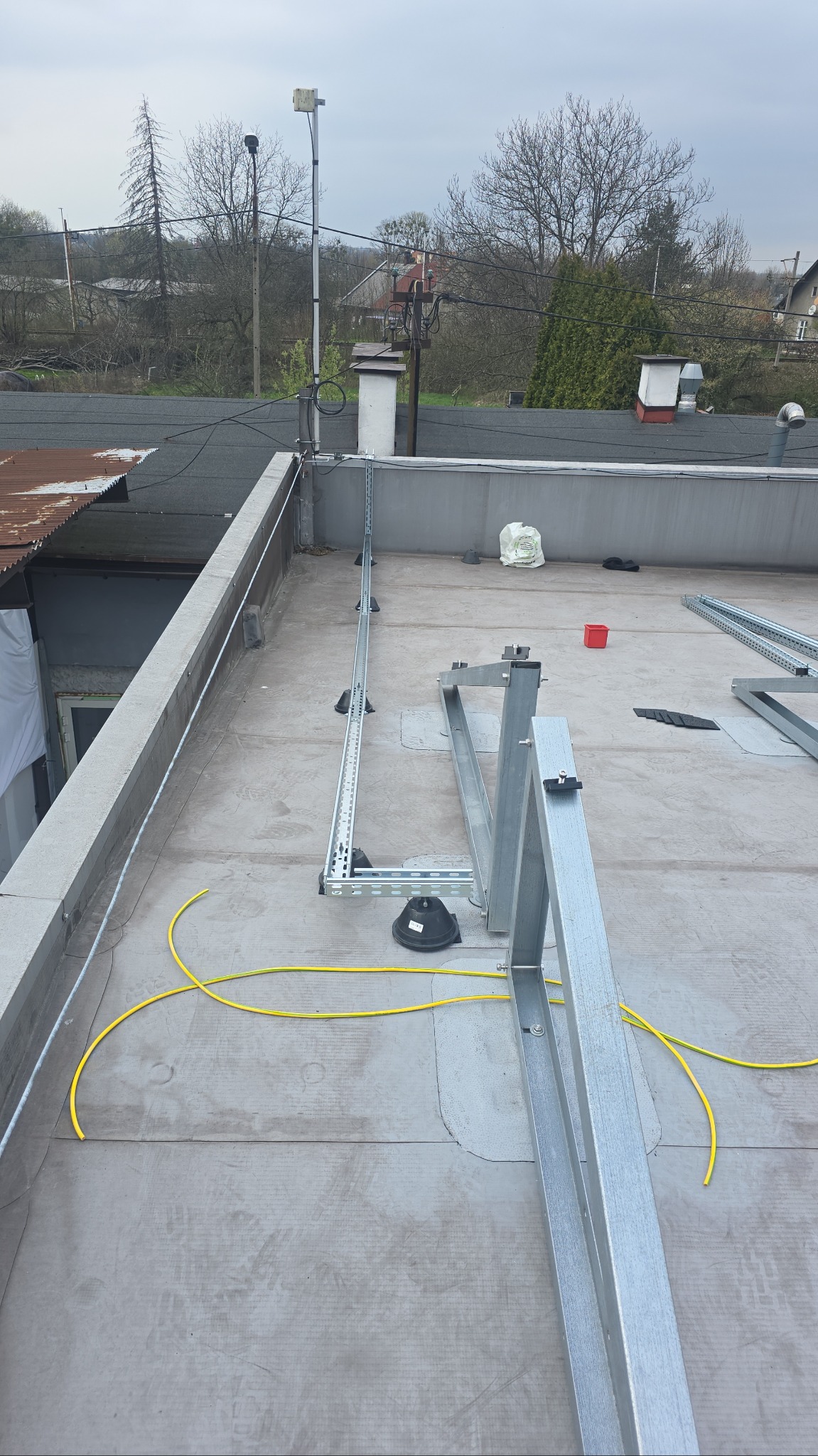 Montaż konstrukcji wsporczej pod panele fotowoltaiczne na płaskim dachu. Widoczne metalowe profile, kable i elementy mocujące. Etap instalacji przed montażem paneli.
