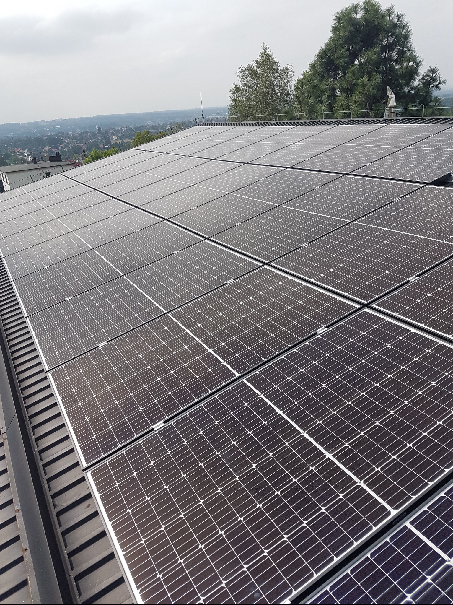 Panel słoneczny na dachu z widokiem na miasto w tle. Instalacja fotowoltaiczna z bliska, równomiernie rozmieszczone moduły.