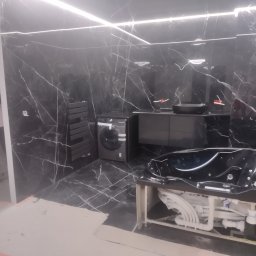 Tomasz Dąbrowski Arsen Usługi Glazurnicze - Nowoczesna łazienka w czerni: marmurowe płytki, wanna z hydromasażem w trakcie montażu, umywalka i pralka. Oświetlenie ledowe na suficie.