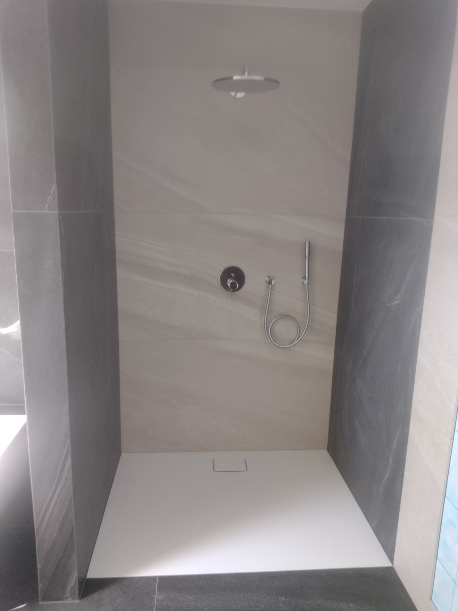 Nowoczesna kabina prysznicowa z odpływem liniowym, wykończona płytkami w odcieniach szarości i beżu, z deszczownicą sufitową i baterią termostatyczną.