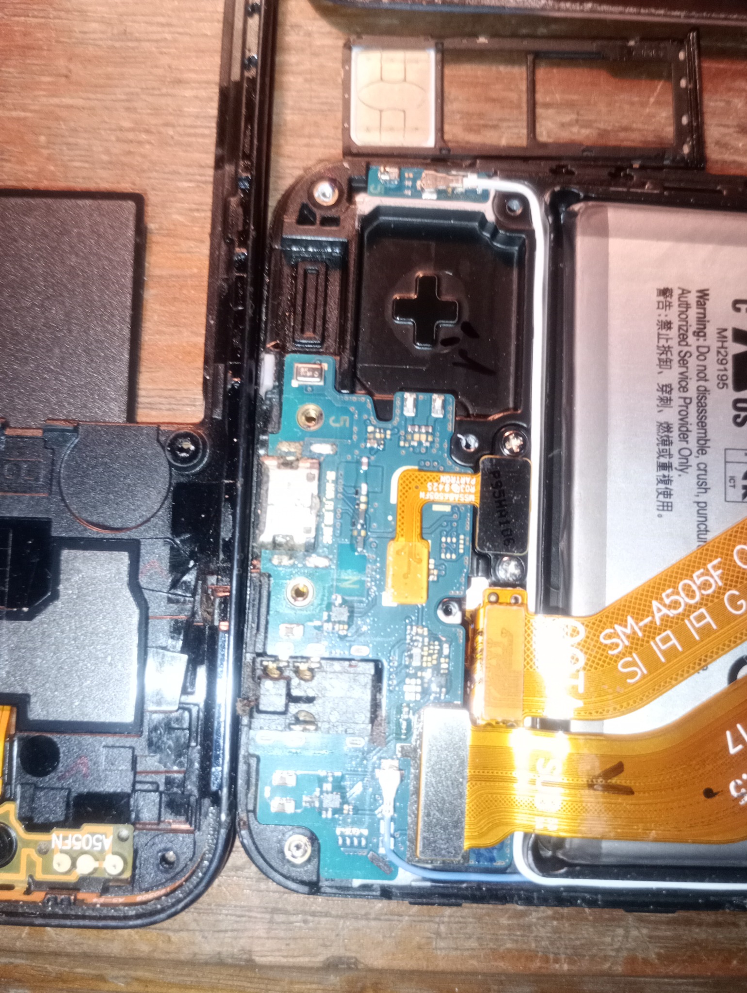 Rozłożony smartfon Samsung A505F z widoczną płytą główną, złączami i baterią. Widoczne ślady naprawy, drobne zabrudzenia. Układ elementów, zbliżenie na wnętrze urządzenia.