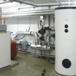 Nowoczesna kotłownia z dwoma piecami De Dietrich i zbiornikami buforowymi, rury w żółtej izolacji, instalacje w pomieszczeniu technicznym.