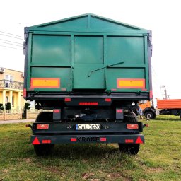 Spaw-Mat Mateusz Osiński - Zielona naczepa z tablicą rejestracyjną CAL 3G20 marki Krone, widziana z tyłu na trawiastym terenie, z fragmentem budynku i innymi pojazdami w tle.