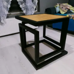 Nowoczesny, spawany stolik kawowy z czarną, stalową ramą i blatem z jasnego drewna. Geometryczna konstrukcja w pokoju.