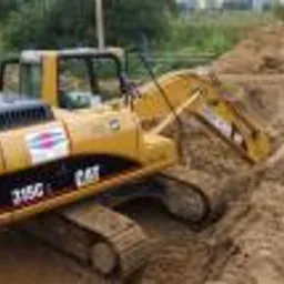 Żółta koparka CAT 315C w wykopie z piasku, widoczne logo firmy na maszynie.