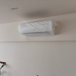 Majuko Sp. z o.o. - Biały klimatyzator Bosch w folii ochronnej, zamontowany na jasnej ścianie. Widoczne przygotowane otwory na kable i instalację elektryczną.