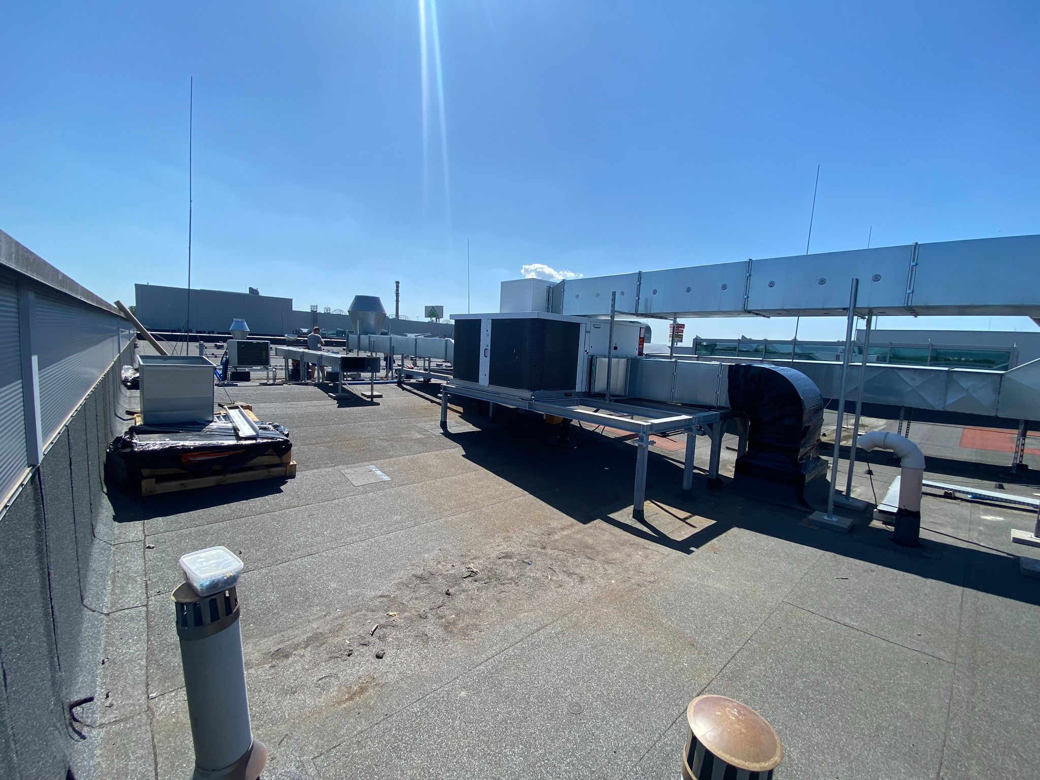 Instalacja wentylacyjna na dachu budynku w słoneczny dzień. Widoczne kanały wentylacyjne, klimatyzatory i elementy montażowe. Dach pokryty papą.