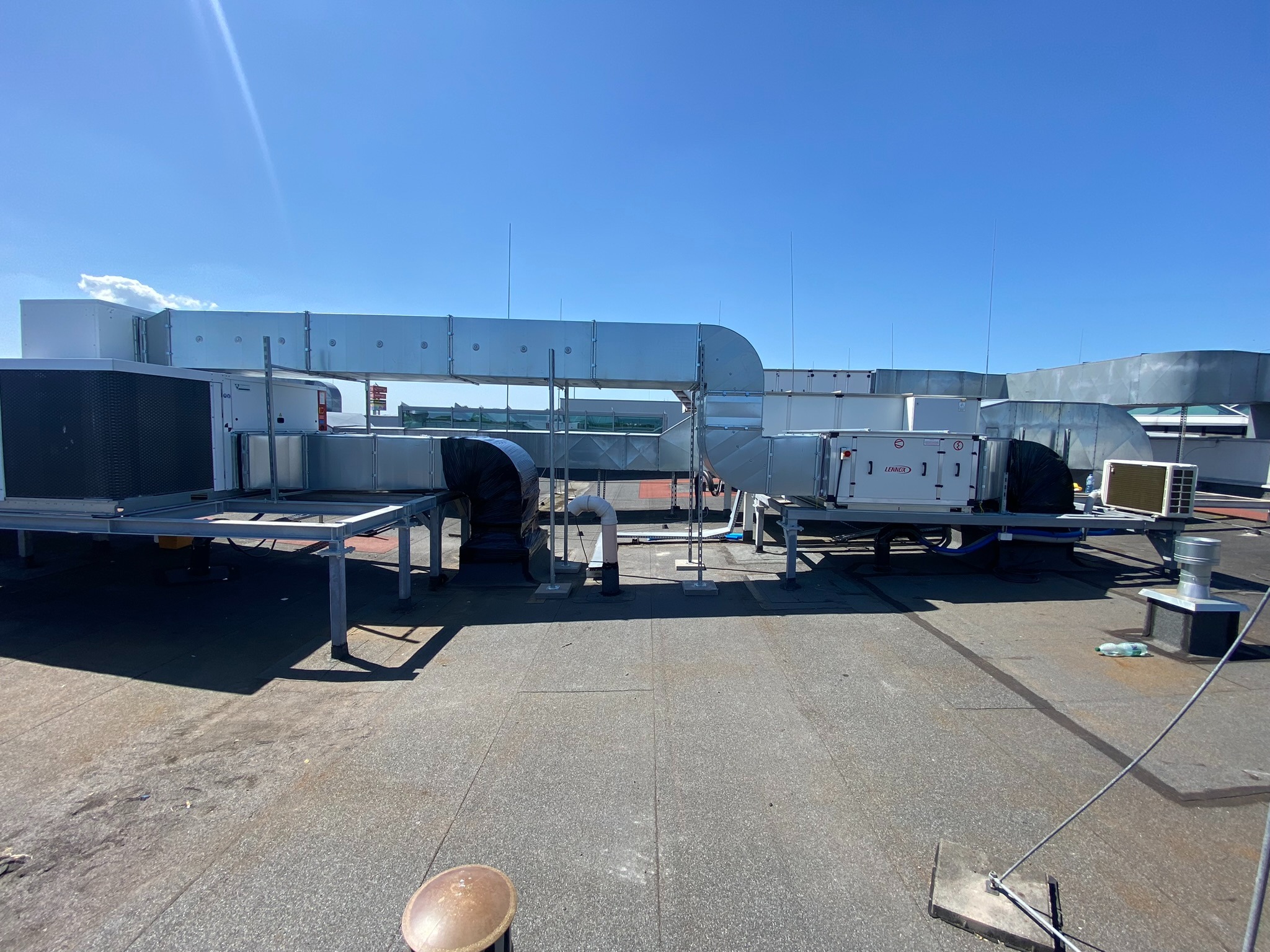 Instalacja wentylacyjna na dachu budynku, widoczne kanały wentylacyjne, klimatyzatory i elementy montażowe w słoneczny dzień. Widok z góry na płaski dach.