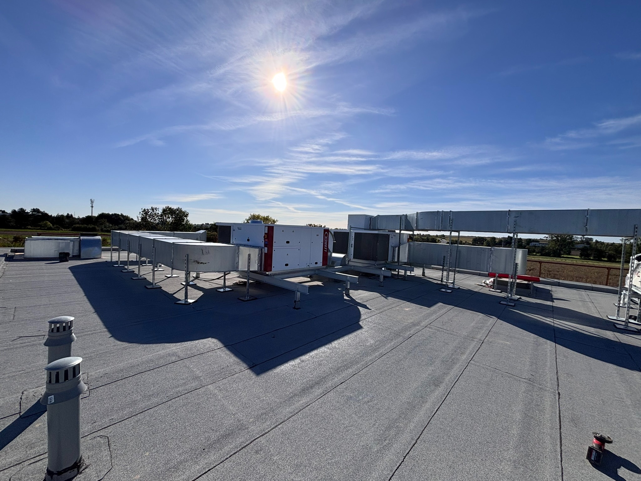 Instalacja wentylacyjna na dachu budynku w Zduńskiej Woli, widok z góry, słoneczny dzień. System kanałów wentylacyjnych i centrala wentylacyjna na płaskim dachu.