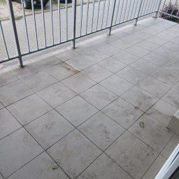 Novo Prime Mariana Rak - Brudna, wykafelkowana podłoga balkonu z widocznymi śladami stóp i zabrudzeniami. W tle barierka i zaparkowane samochody.