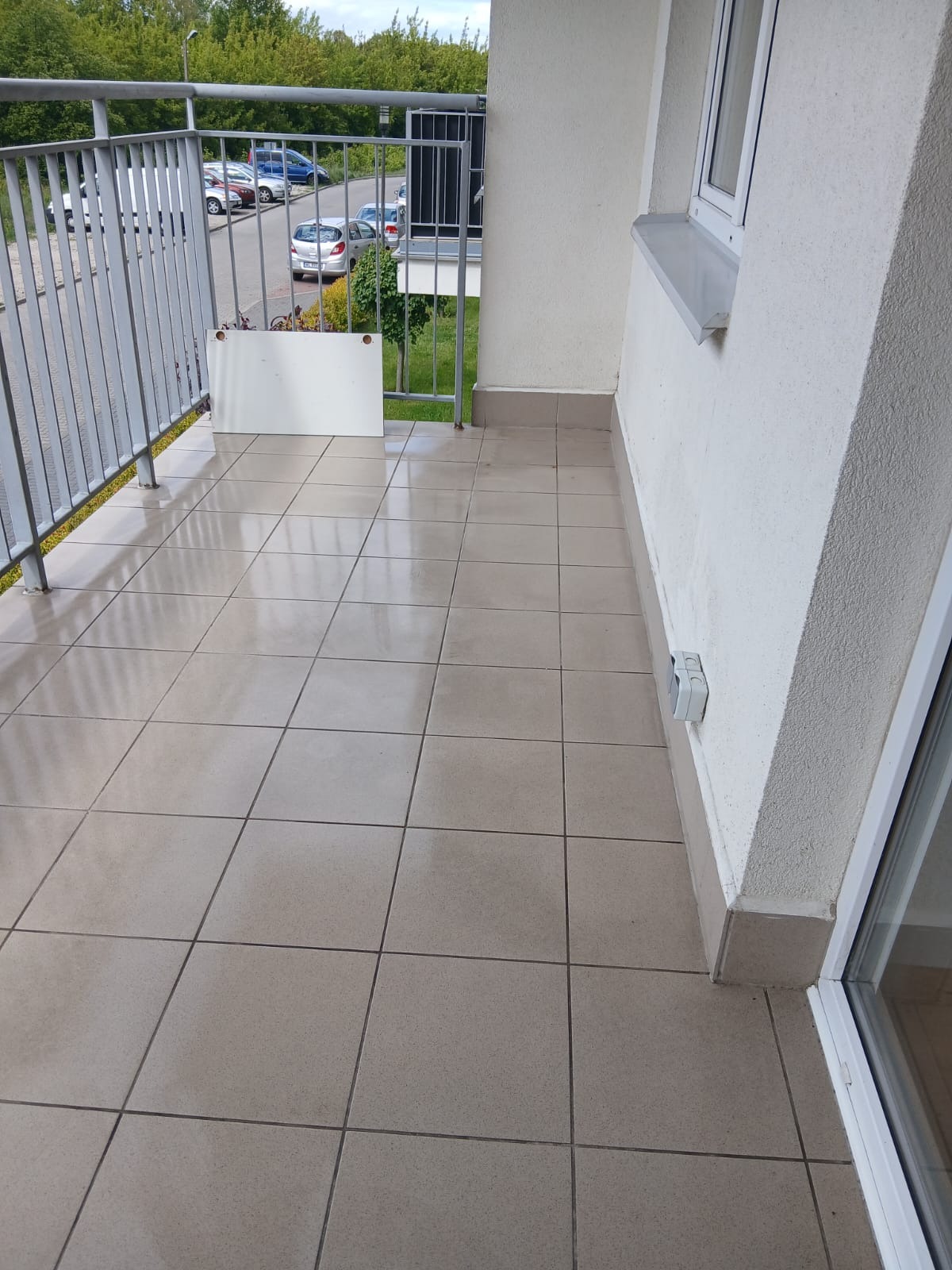 Błyszcząca, beżowa podłoga z płytek na balkonie z metalową barierką. Widok na zewnątrz przez barierkę. Świeżo umyta podłoga.