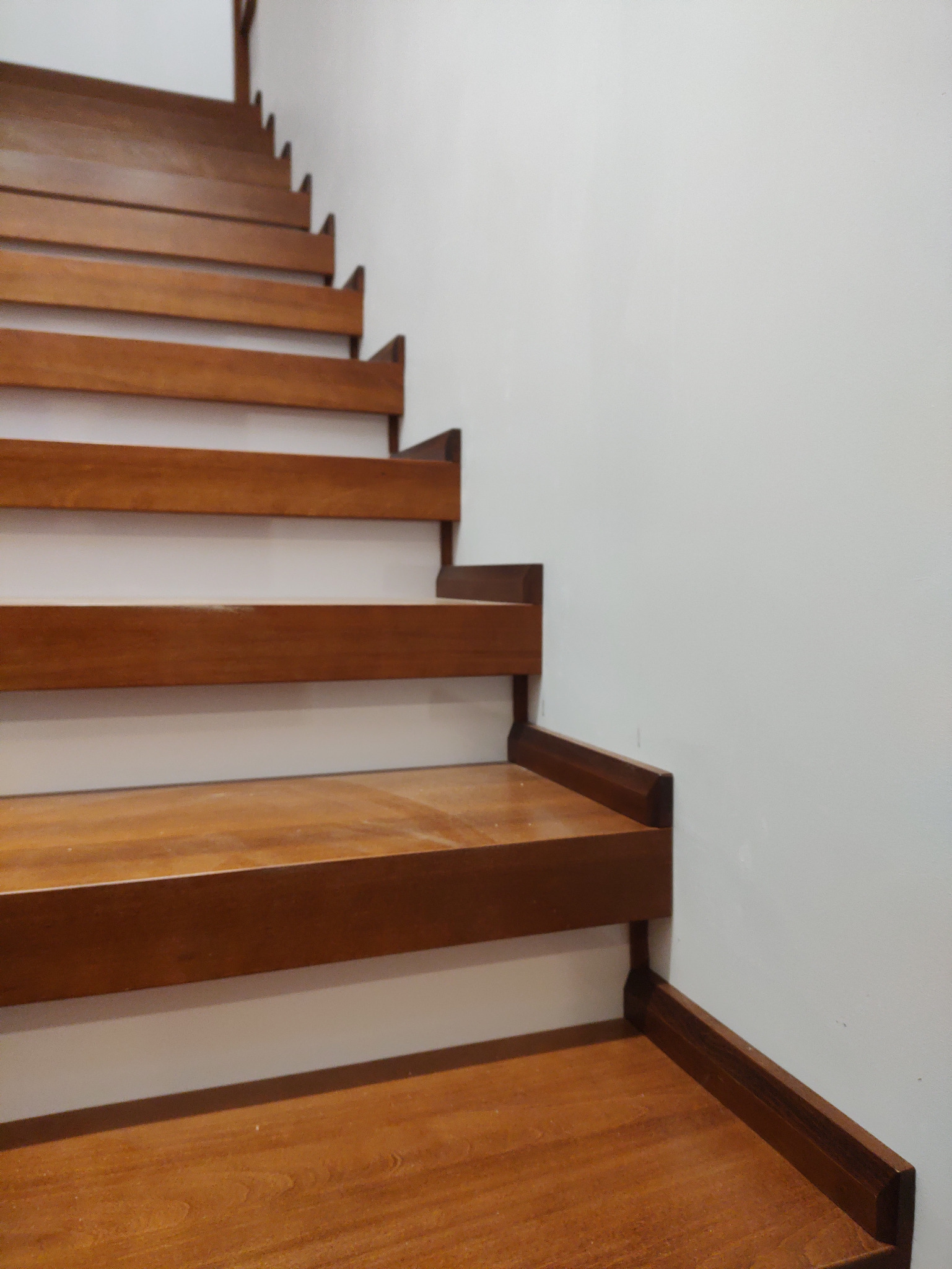 Detal brązowych, drewnianych schodów z widoczną strukturą drewna, na tle białej ściany. Minimalistyczny design.