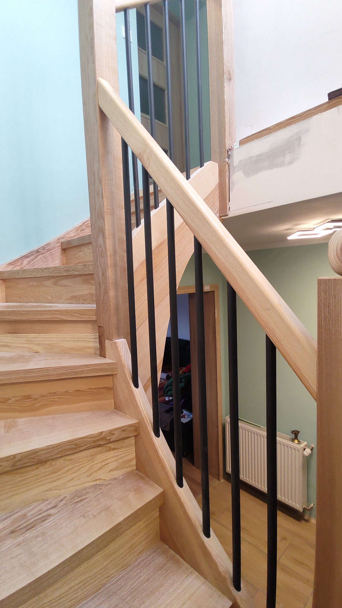Jasne drewniane schody z czarnymi, metalowymi balustradami. Widoczne detale wykończenia i naturalna tekstura drewna. Ujęcie z dołu, podkreślające solidność konstrukcji.