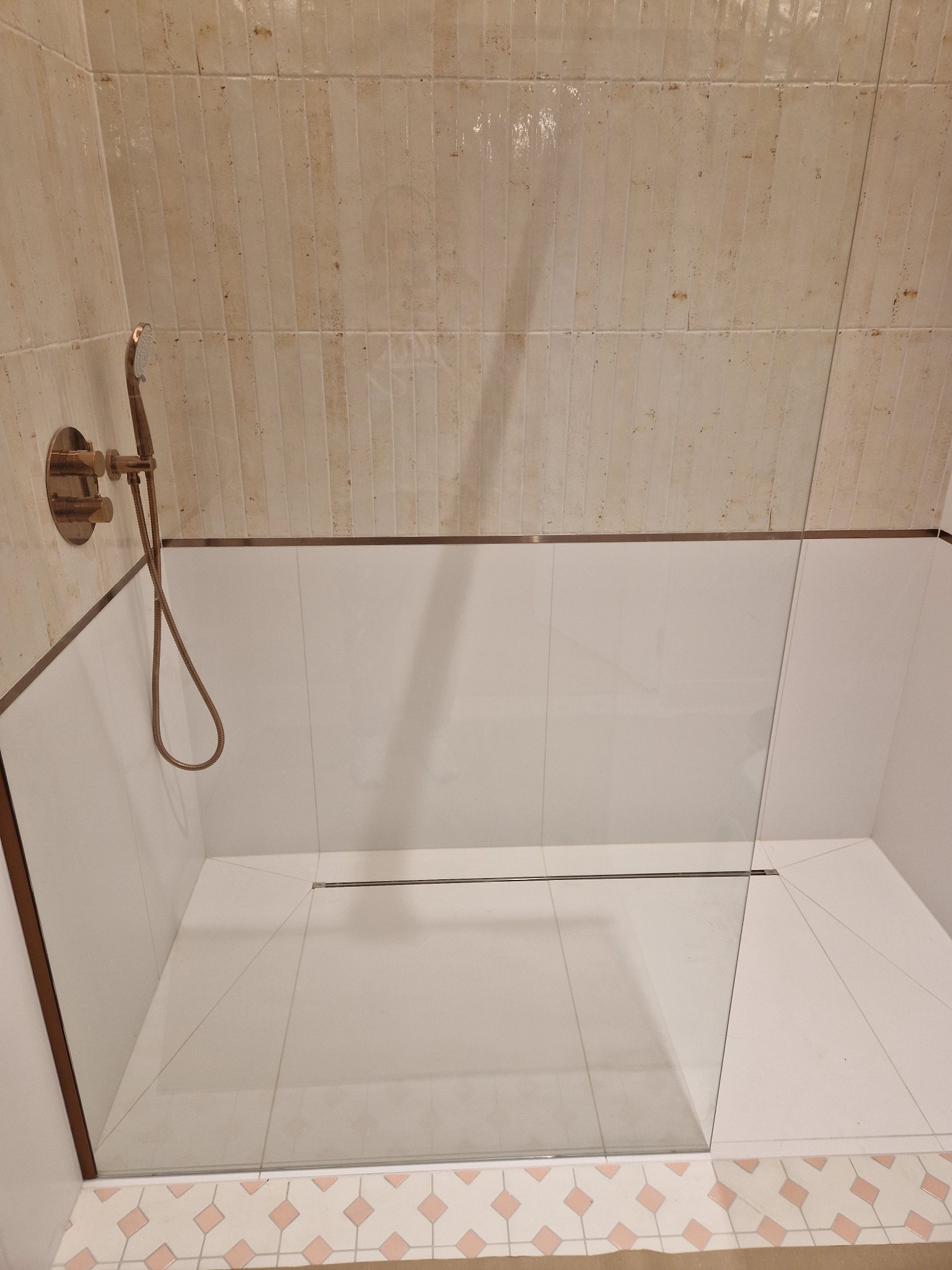 Kabina prysznicowa walk-in z odpływem liniowym, wykończona beżowymi płytkami na ścianach i podłodze, z armaturą w kolorze różowego złota. Widoczna szklana ściana.