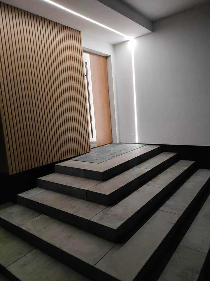 Nowoczesne schody wejściowe z kostki brukowej, drewniana okładzina ścienna i subtelne oświetlenie LED tworzą eleganckie wejście do budynku.