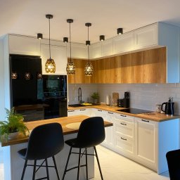 Livaro Meble - Nowoczesna kuchnia: białe szafki z drewnianymi akcentami, czarne sprzęty AGD i wyspa z hokerami na tle marmurowej podłogi, oświetlona wiszącymi lampami.
