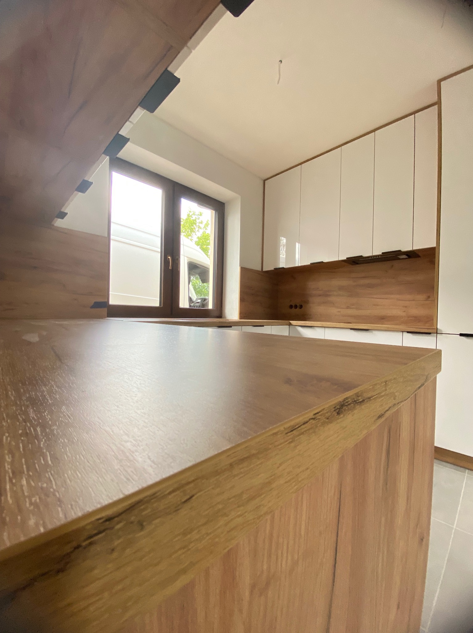 Nowoczesna kuchnia z drewnianym blatem i białymi szafkami, widok z dołu,  okno w tle,  minimalistyczny design.