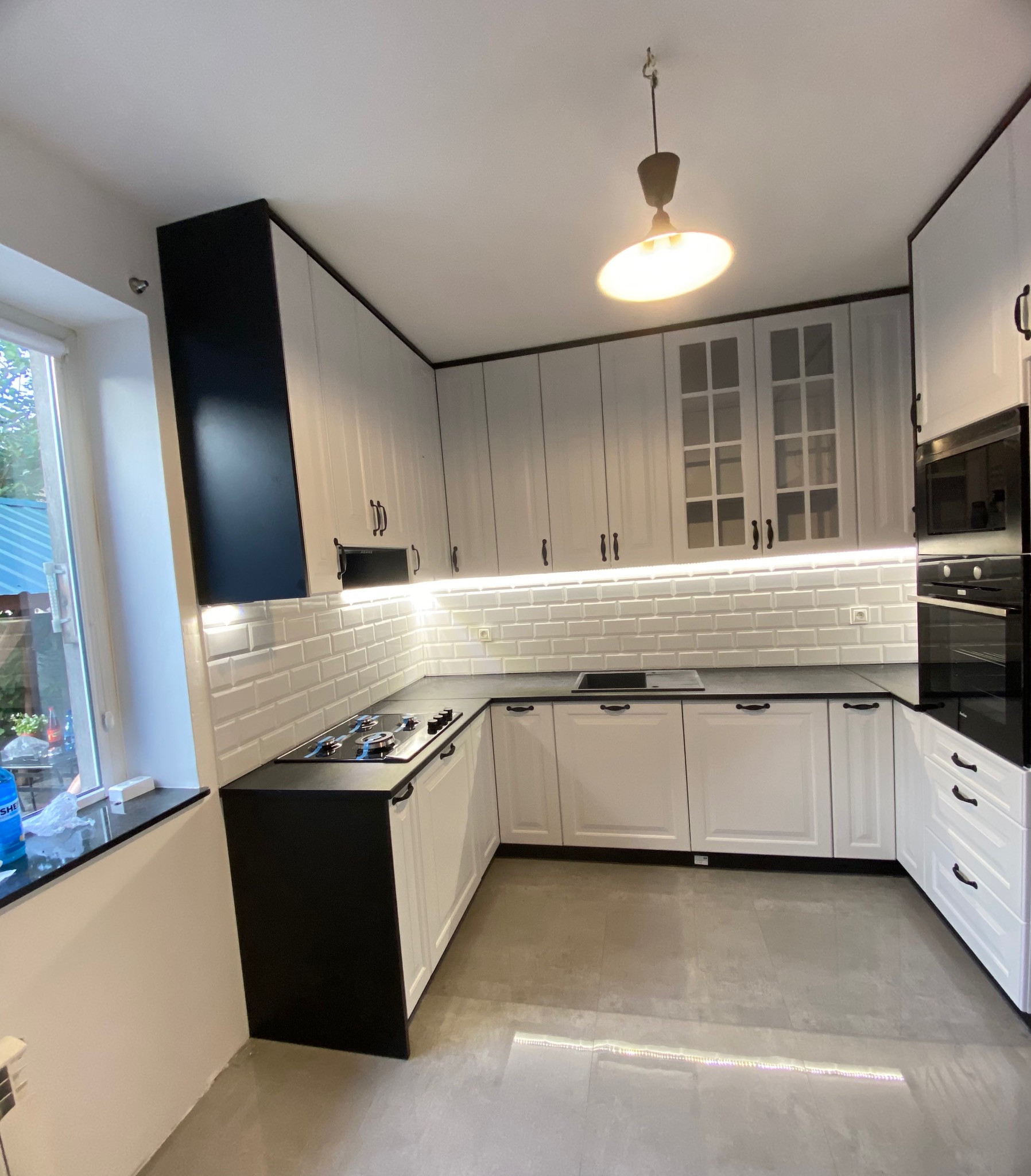 Czarno-biała kuchnia z frezowanymi frontami, czarnymi blatami i uchwytami. Podświetlenie LED nad blatem. Widok na okno i fragment ogrodu.