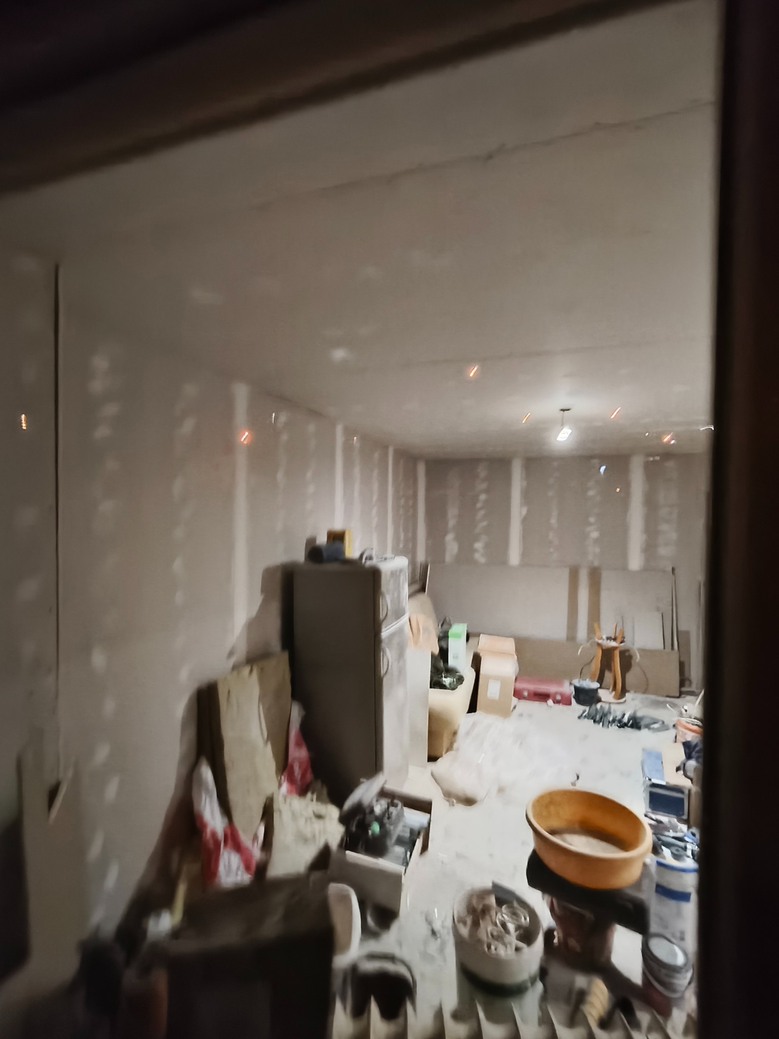 Wnętrze w trakcie prac wykończeniowych: ściany obłożone płytami karton-gips, widoczne narzędzia i materiały budowlane, sufit z instalacją oświetleniową, bałagan.