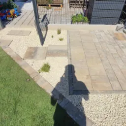 Ukończona ścieżka z kostki brukowej i kamienia ozdobnego w ogrodzie, widok z góry. Częściowo widoczna postać w trakcie prac wykończeniowych.