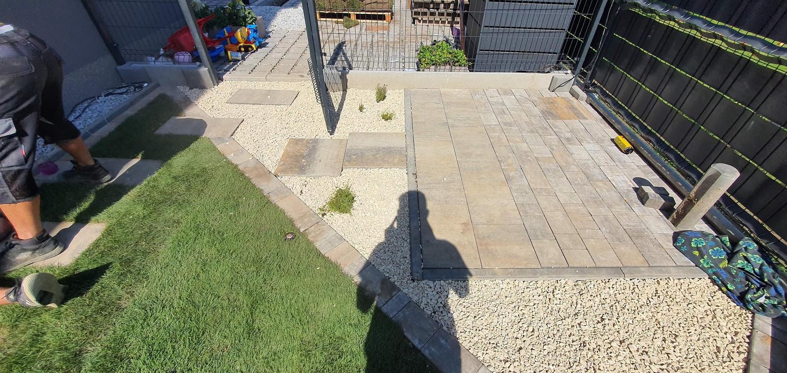 Ukończona ścieżka z kostki brukowej i kamienia ozdobnego w ogrodzie, widok z góry. Częściowo widoczna postać w trakcie prac wykończeniowych.