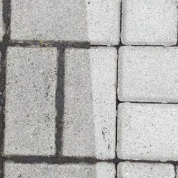 KostkaBezPodjazdu - Częściowo wyczyszczona, szara kostka brukowa. Po lewej stronie widoczny brud i mech, po prawej czysta powierzchnia. Układ pionowy.
